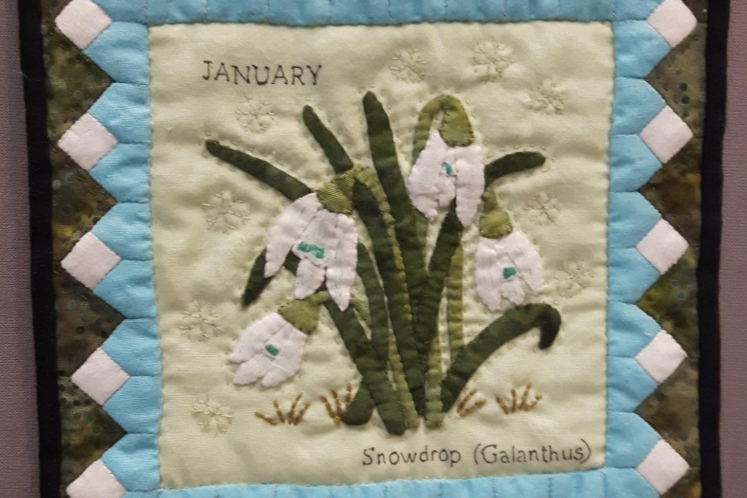 Miniature quilt depicting snowdrops growing on a cream background with a blue and white border