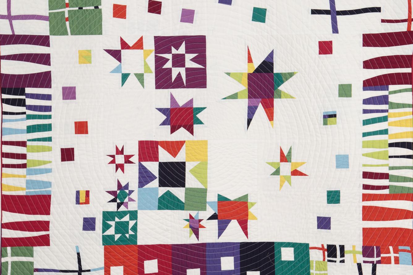 Beige quilt with rainbow coloured pattern in triangles, rectangles and squares