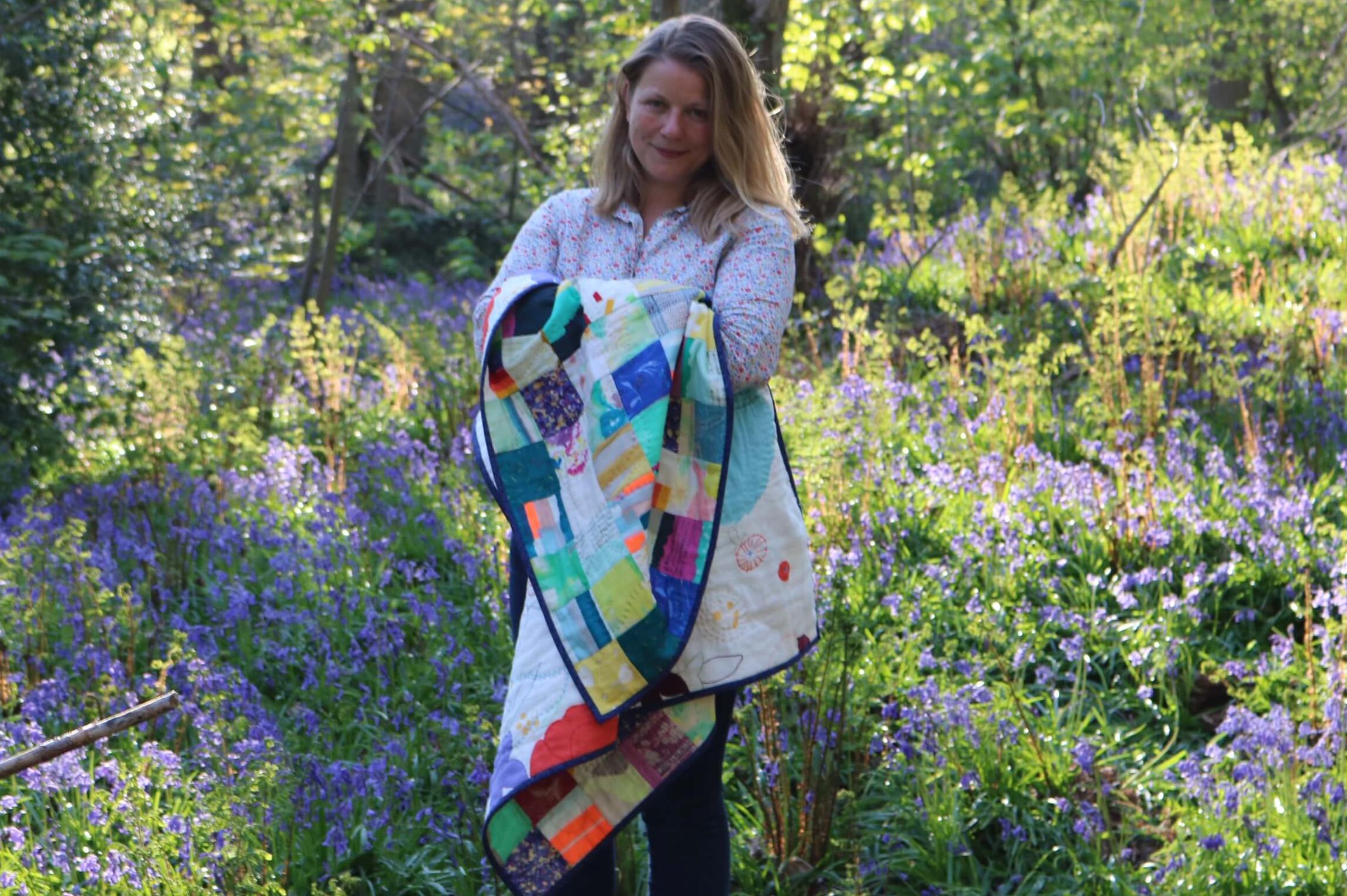 Jenni holding a quilt in a field of bluebells