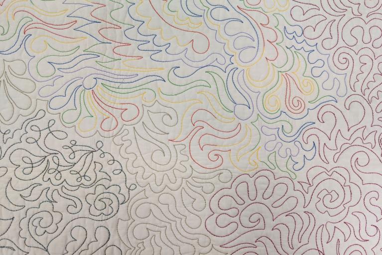 Beige wholecloth quilt with a pattern of swirls and curves in rainbow coloured thread