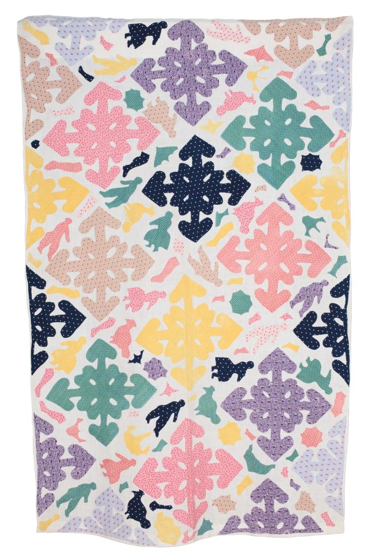 A cot coverlet made from colourful printed cotton shapes which have been applied to a single cotton sheet foundation fabric.