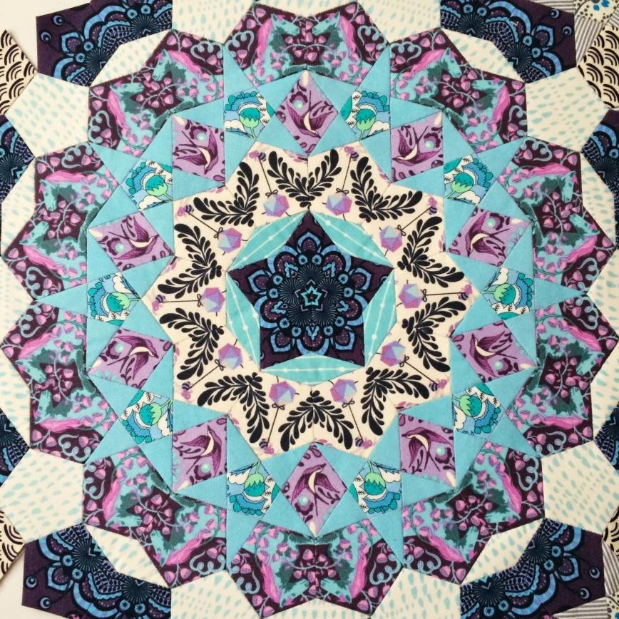 Close up of a quilted star piece made of turquoise and pink patterned fabric in triangular and pentagonal shapes