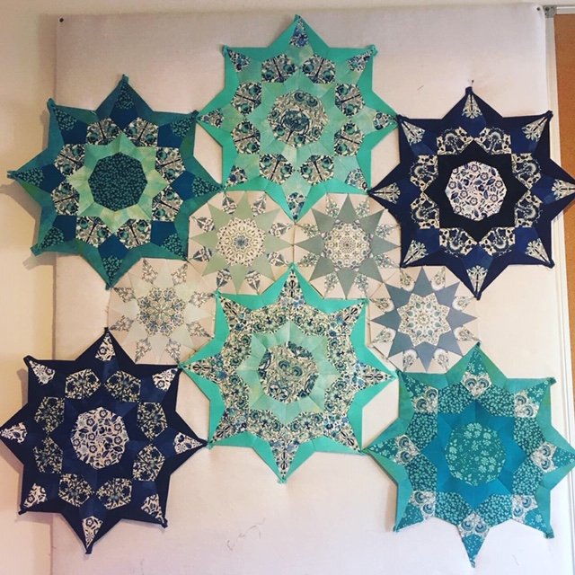 Blue, turquoise, green and navy patterned star shaped quilt pieces laid out in a connecting pattern