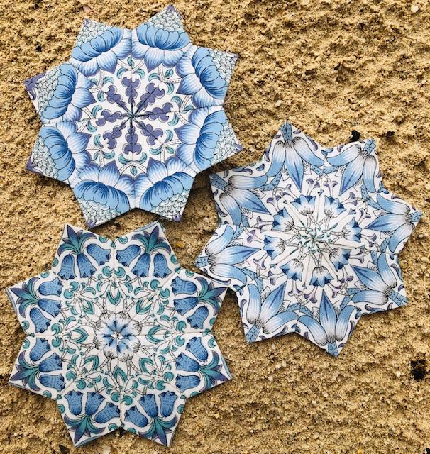 Close up of 3 star shaped quilt pieces in light blue patterned fabric on a brown background