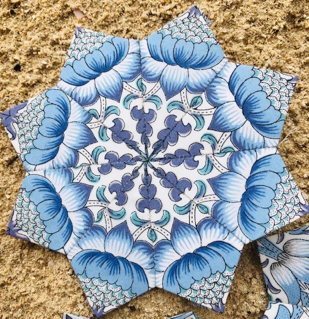 Close up of a star shaped quilt piece in light blue patterned fabric on a brown background