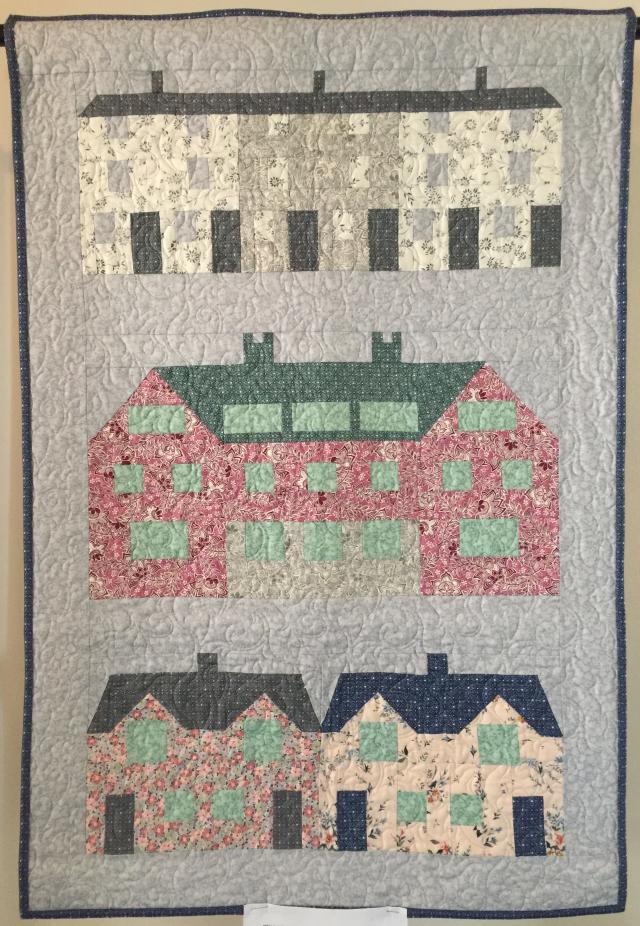 Quilt with light background and dark border depicting rows of houses in patterned fabric