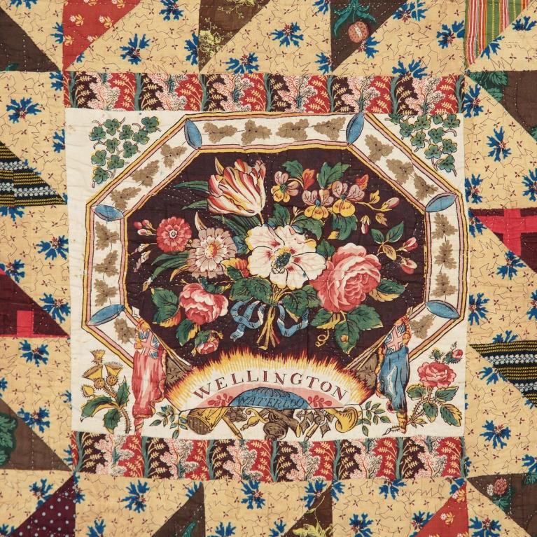 Quilt with floral design and the words Wellington and Waterloo in the centre with a repeated pattern of triangles made of patterned fabric round the edges