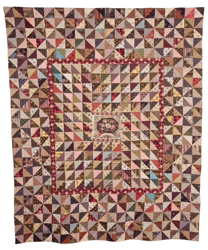 Large quilt with repeated triangles made of different patterned fabrics, in the centre a floral design and the word Wellington