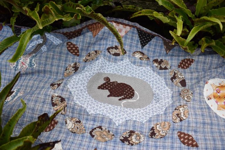Quilt with blue check pattern background and mouse in a grey circle in the middle