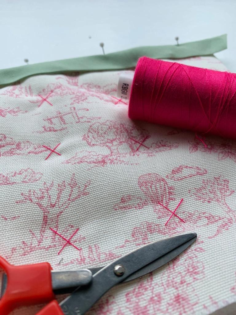 Scissors and a reel of thread laid on a piece of beige fabric with a pink tree pattern