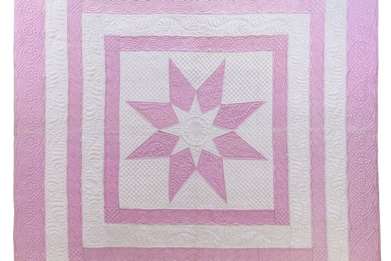Quilt with a pink star in the centre of concentric pink and white squares