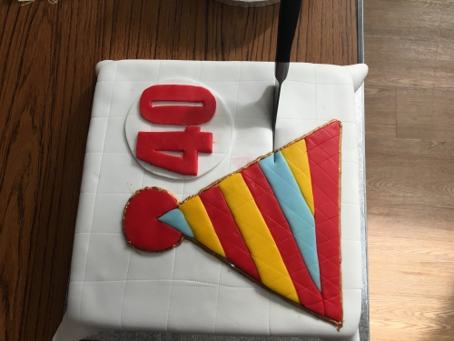 Square cake with white icing, decorated with a stripy red, yellow and blue icing hat and red number 40