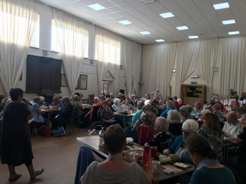Woman with microphone speaking to hall full of people sat at tables