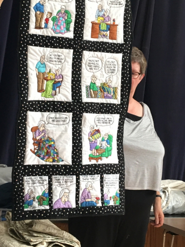 Woman holding up quilt depicting a cartoon strip