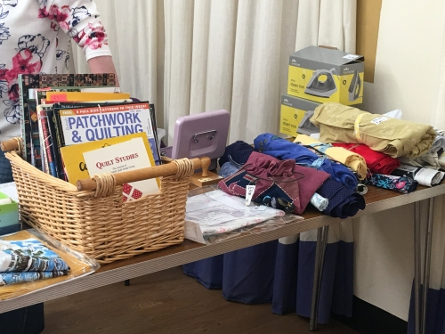 Selection of quilting magazines in a basket on a table next to a selection of fabrics
