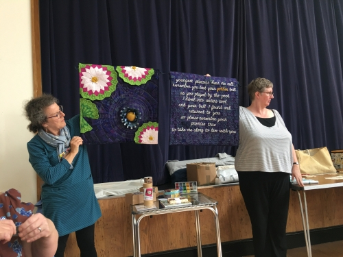 Two ladies holding up quilt with waterlily design and some text