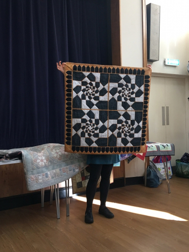 Woman holding up quilt with gold triangle pattern border and a black and white geometric pattern