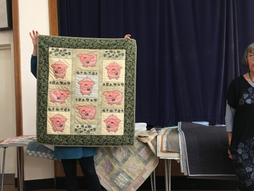 Quilt with green border and repeating pattern of pink pigs in beige squares