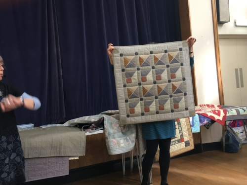 Woman holding up quilt with geometric pattern in ochre, greys and white