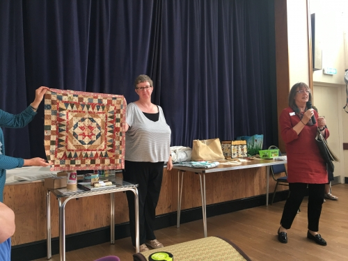Woman holding up quilt with red, blue and beige triangle pattern