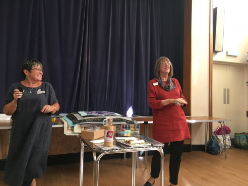 2 woman standing in front of crowd next to a table