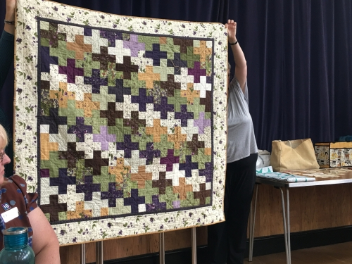 Quilt with beige floral patterned border and design of crossed in greens, yellows, navys and whites