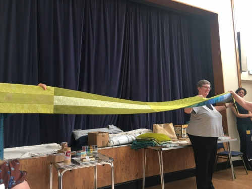 People holding end of very long and narrow quilt with green back design