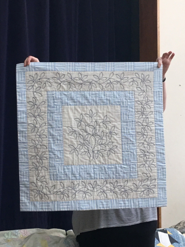 Quilt with embroidered vine pattern on a cream background with blue borders