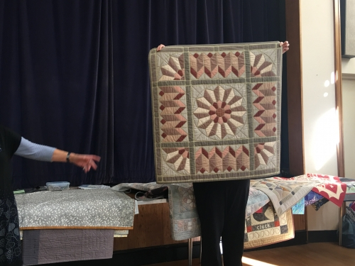 Woman holding up a quilt with green borders and a radial pattern of geometric shapes in pinks
