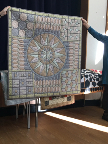 Large quilt with compass star pattern surrounded by geometric shape blocks in blues and pinks