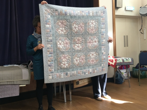 Women holding up large quilt with light blue and pink floral design
