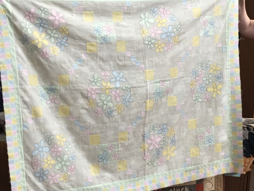 Quilt with pastel coloured flowers and squares on a beige neutral background