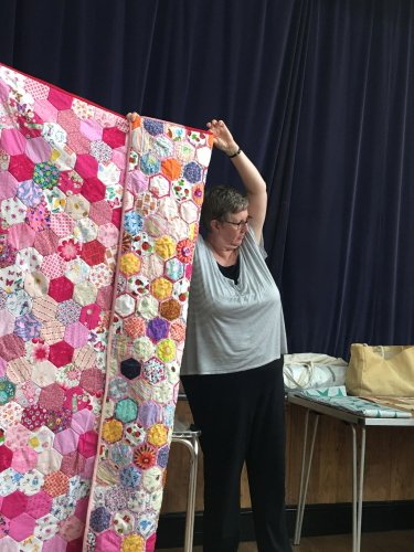 Women holding up large quilt made of multi-coloured hexagonal pieces showing pink back