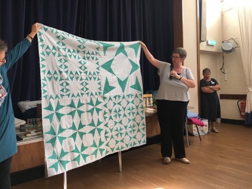 Woman with microphone holding up green and white star patterned quilt