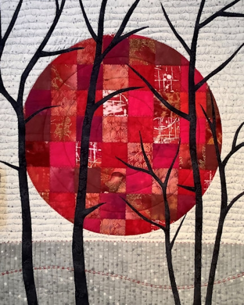 Quilt with beige and grey background with large red circle made of squares of different red squares with dark branches in the foreground