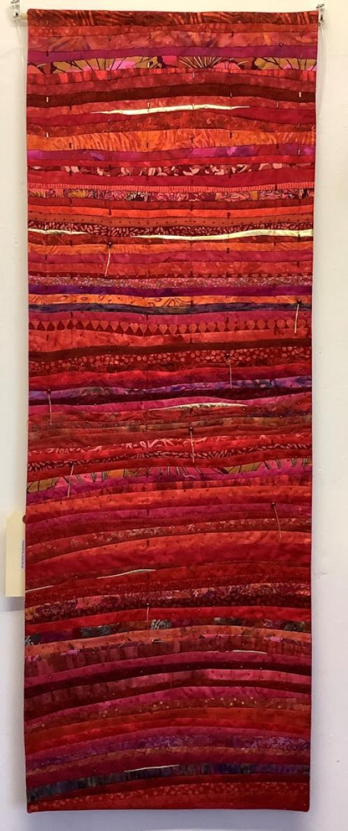 Narrow rectangular quilt made of thin stripes of different shades of red and pink