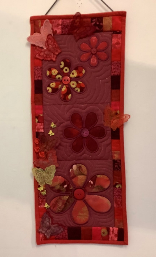 Narrow rectangular quilt made of different shades of red fabric with a flowers and butterflys design