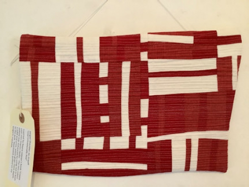 Small quilt hung on wall made up of red and white rectangular shapes