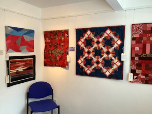 A collection of red themed quilts displayed on a gallery walls