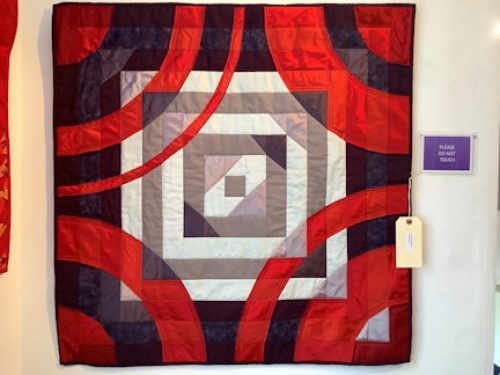 Square quilt with grey and white concentric squares in centre, overlayed with red concentric circles on a dark background