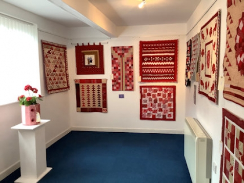 A collection of red themed quilts displayed on a gallery walls