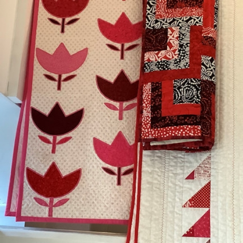 A selection of folded red and white themed quilts