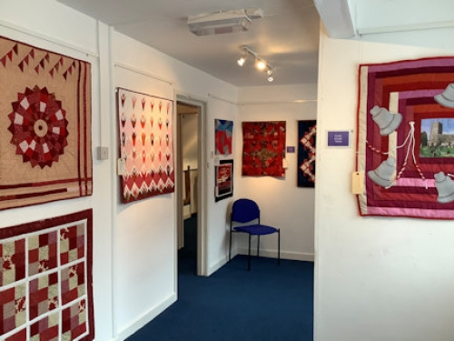 A collection of red themed quilts displayed on a gallery walls