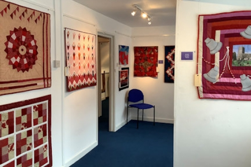 A collection of red themed quilts displayed on a gallery walls