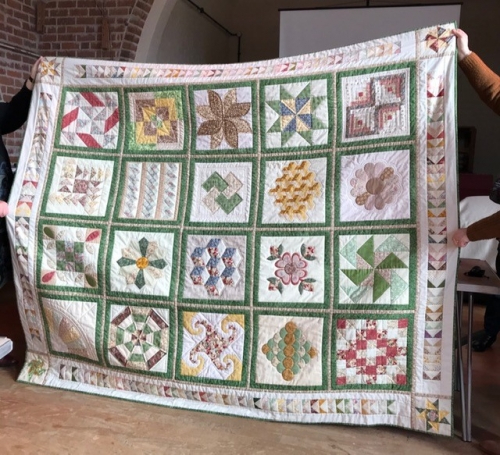 Large traditional sampler quilt with green borders and patterns in muted greens, greys, yellows, blues and pinks