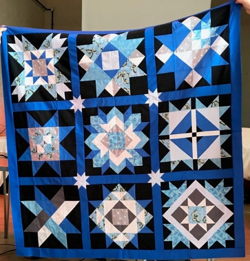 Blue, black and white quilt made of 9 square blocks with star and flowers made of triangles