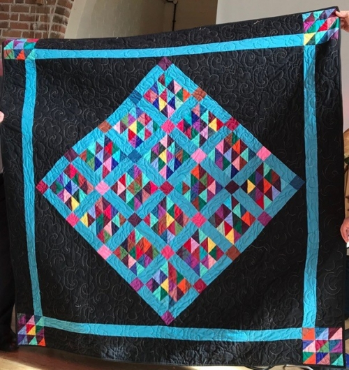 Large black quilt with bright blue border and a large blue diamond pattern in the centre with blue borders and multicoloured triangles