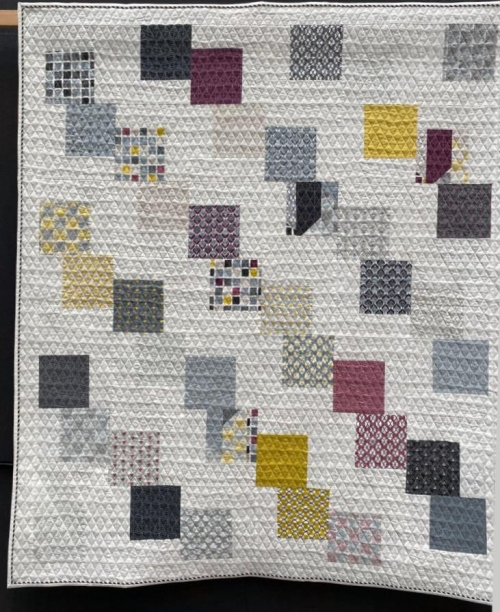 White quilt with random pattern of squares in greys, yellow and dark pinks