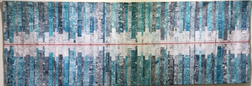 Horizontal rectangular quilt with blue vertical rectangles of different widths and lengths with a red horizontal stripe in the centre.