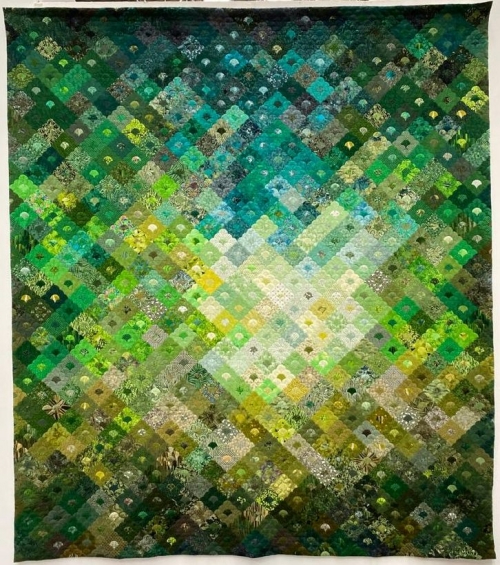 Quilt using greens, yellows and turquoise fabrics in a repeated pattern of small diamonds with a scalloped design